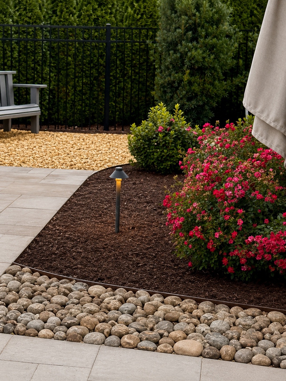 Finished accent landscape featuring flowering shrubs, decorative stone and a clean mulch bed around a patio edge.