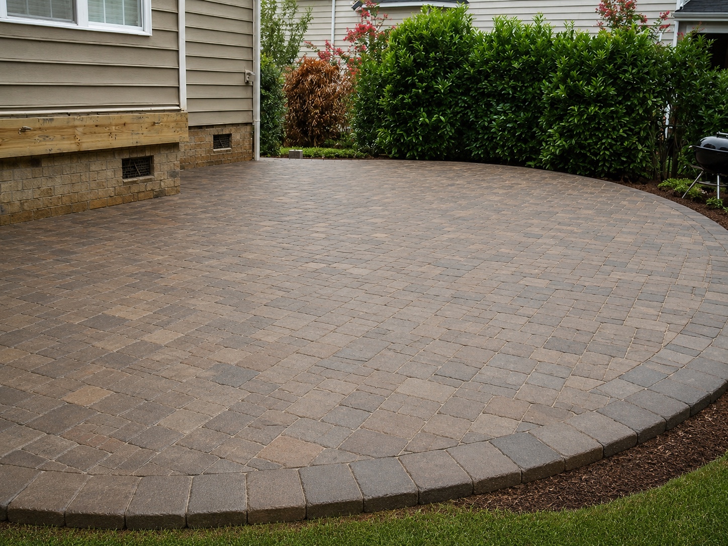 Curved residential paver patio with a clean soldier-course border and landscaped perimeter.